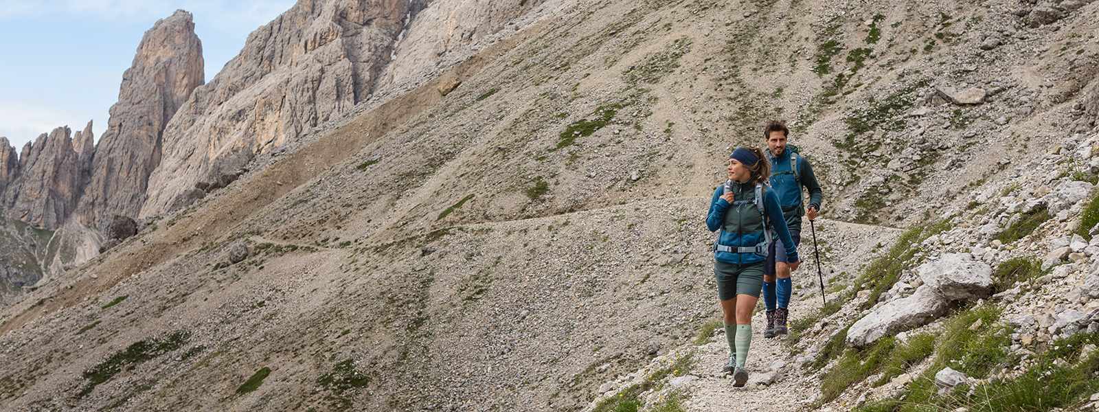 Man and woman hike down a mountain with hiking sticks in hand and carry hiking socks