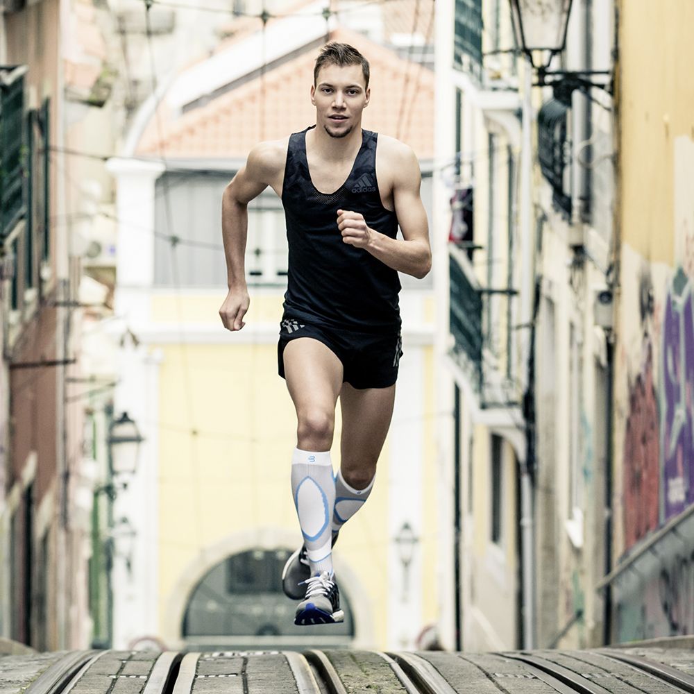 Runners with compression stockings to run runs a hill up to the viewer in a city