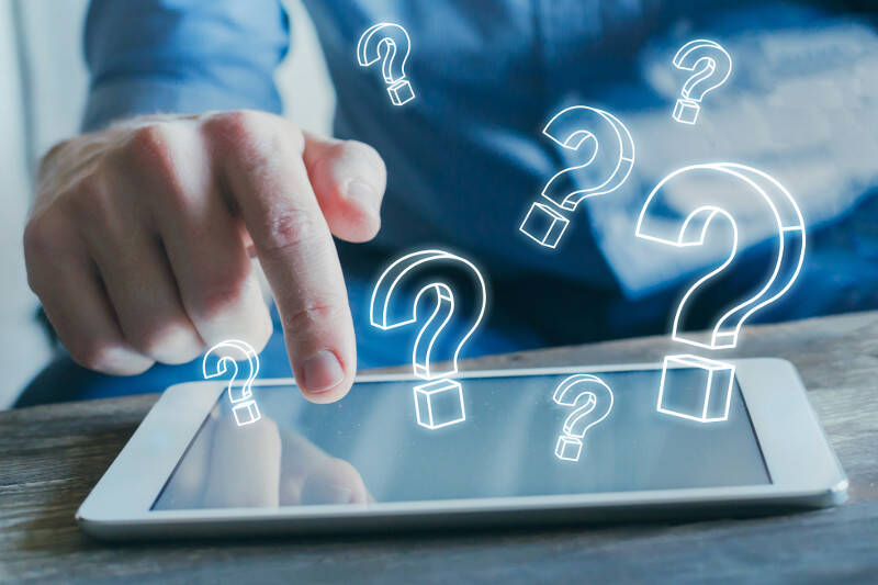Man taps with index finger on tablet display about it are question marks inserted into the picture