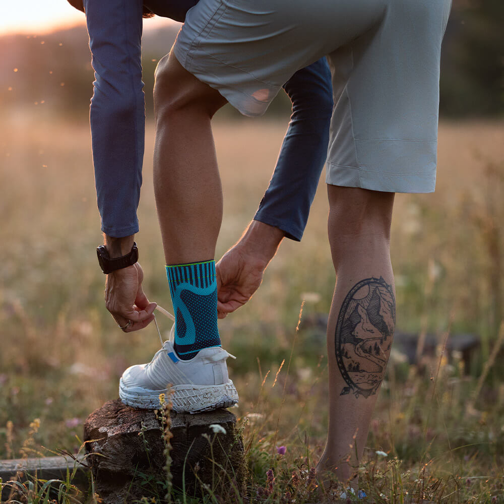 A man puts his foot on a stump and binds his shoe new. He has an Achilles tendon bandage on the left foot