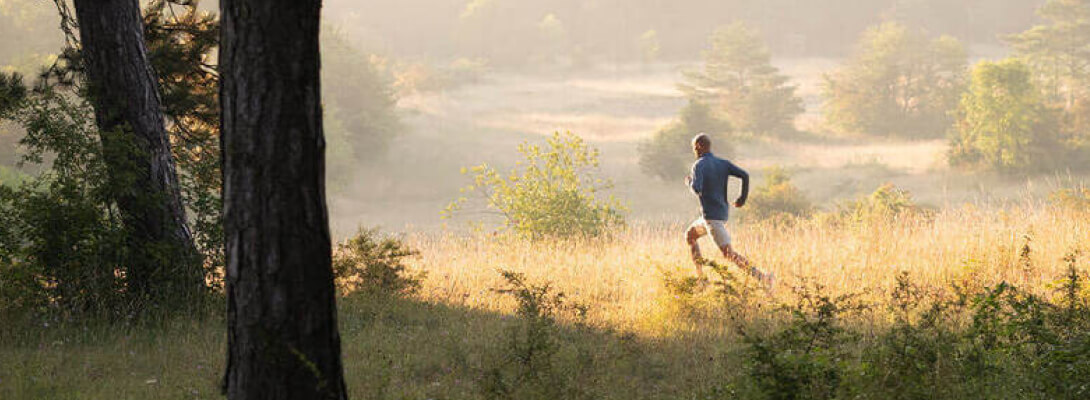 Sports in Sport Outdoor Man jogs over a meadow in the foreground a tree in the background are hills